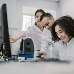 Grupo de pesquisadores trabalha em conjunto diante de um computador em um laboratório moderno.