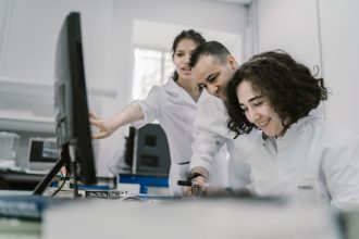 Grupo de pesquisadores trabalha em conjunto diante de um computador em um laboratório moderno.