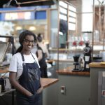 Empreendedora sorrindo atrás do balcão de uma cafeteria, em seu ambiente de trabalho.