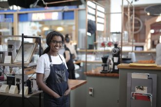 Empreendedora sorrindo atrás do balcão de uma cafeteria, em seu ambiente de trabalho.