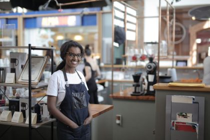 Empreendedora sorrindo atrás do balcão de uma cafeteria, em seu ambiente de trabalho.