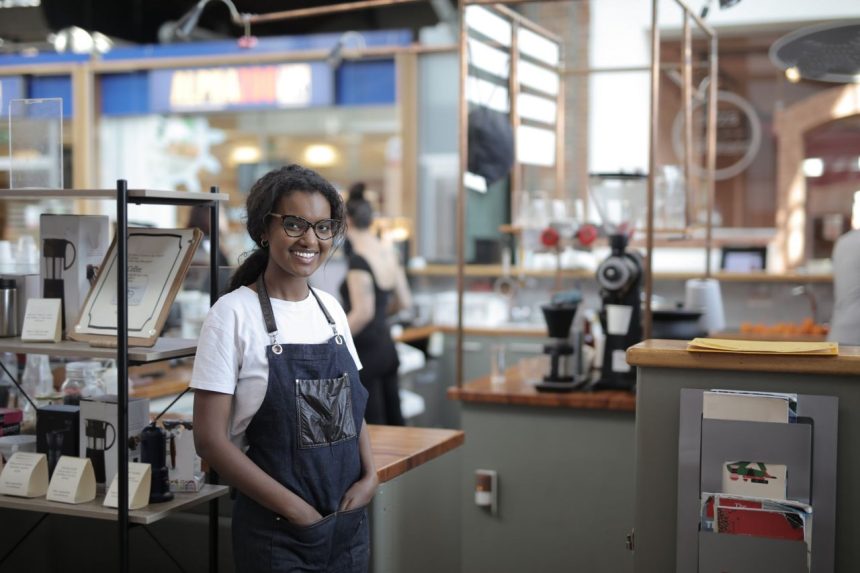 Empreendedora sorrindo atrás do balcão de uma cafeteria, em seu ambiente de trabalho.