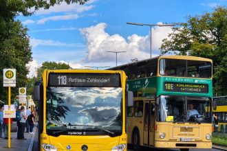 Dois ônibus coloridos parados em um ponto de transporte coletivo em uma rua urbana.