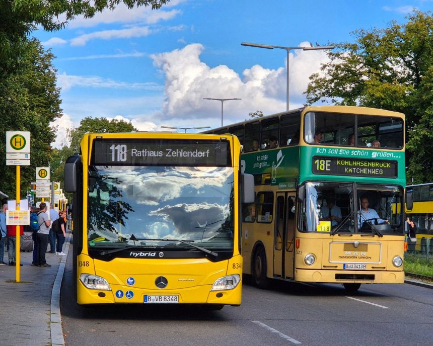 Dois ônibus coloridos parados em um ponto de transporte coletivo em uma rua urbana.