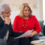 Casal idoso analisa documentos financeiros juntos em casa.