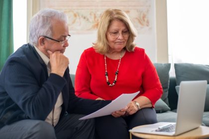 Casal idoso analisa documentos financeiros juntos em casa.