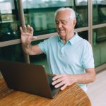 Homem idoso participa de uma chamada de vídeo pelo laptop, sentado em casa.