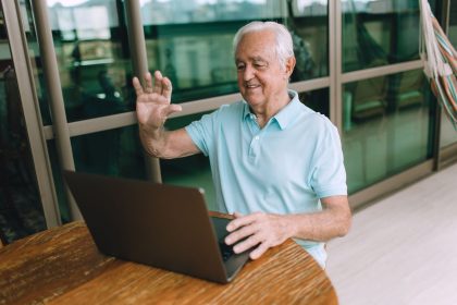 Homem idoso participa de uma chamada de vídeo pelo laptop, sentado em casa.
