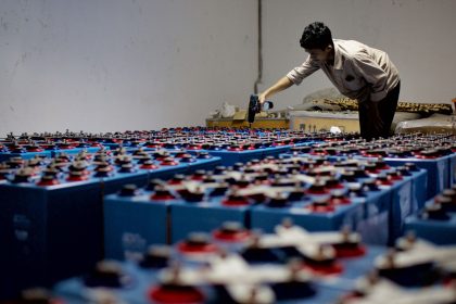Trabalhador inspeciona fileiras de baterias industriais dentro de uma instalação fabril